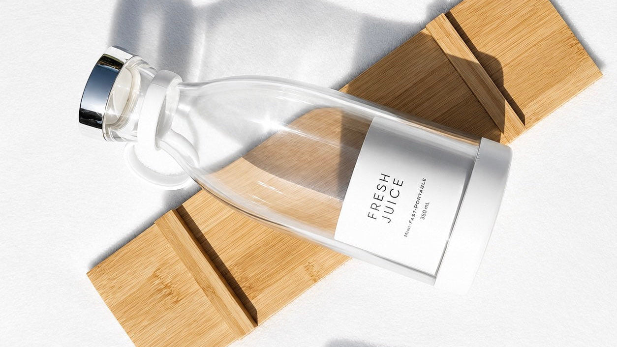 Clear glass bottle labeled 'Fresh Juice' on a wooden block with a white background